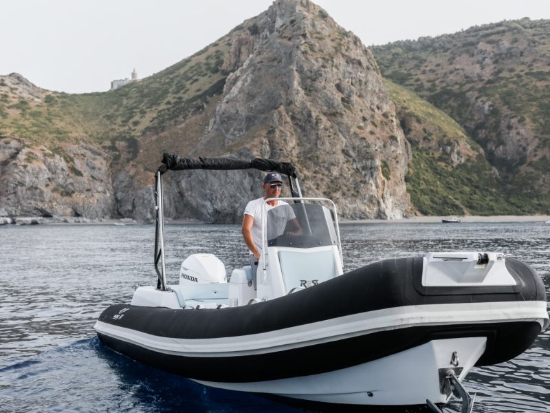Gommone RER Marine 747 ripreso di tre quarti davanti a una costa rocciosa.